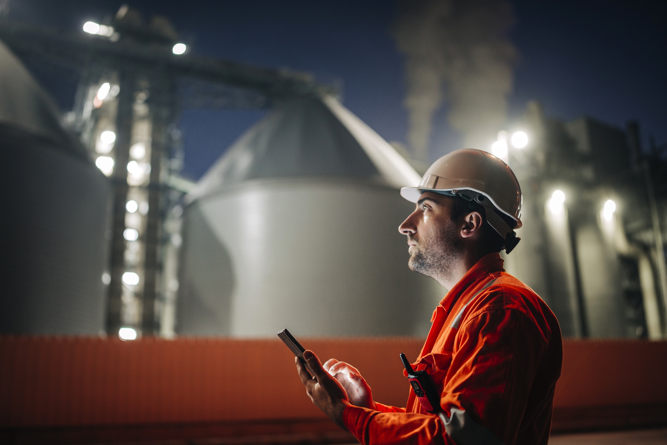 Caucasian man engineer using digital tablet working late night shift at petroleum oil refinery in industrial estate