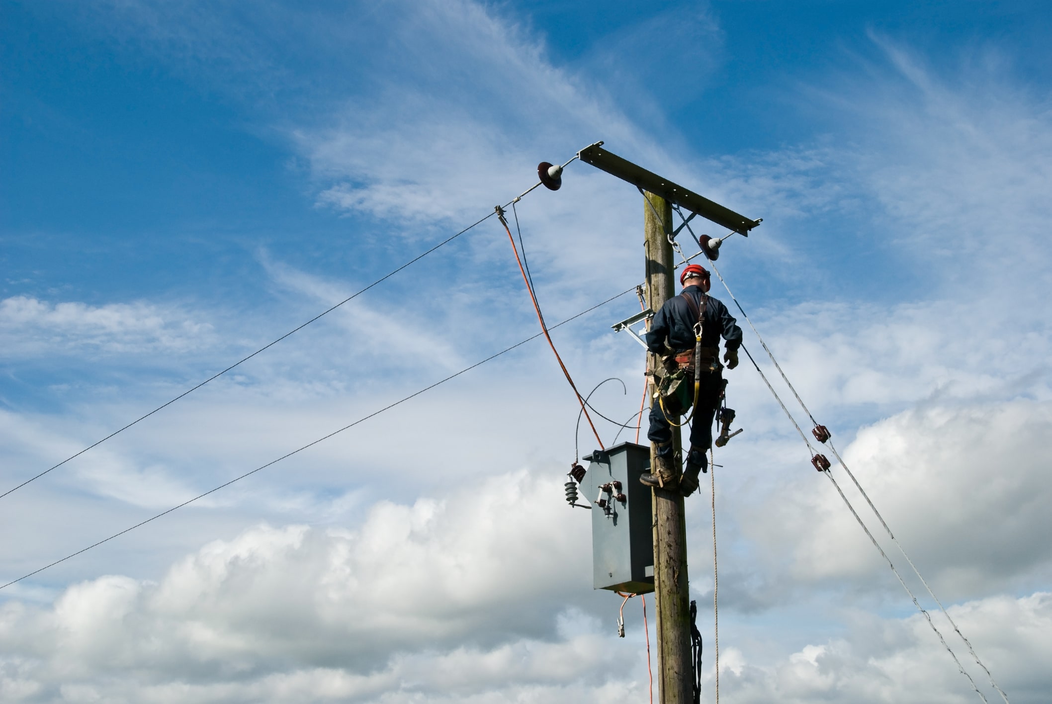 An unrecognisable utility workman carries out repairs on a transformer connected to an 11000 volt power line.