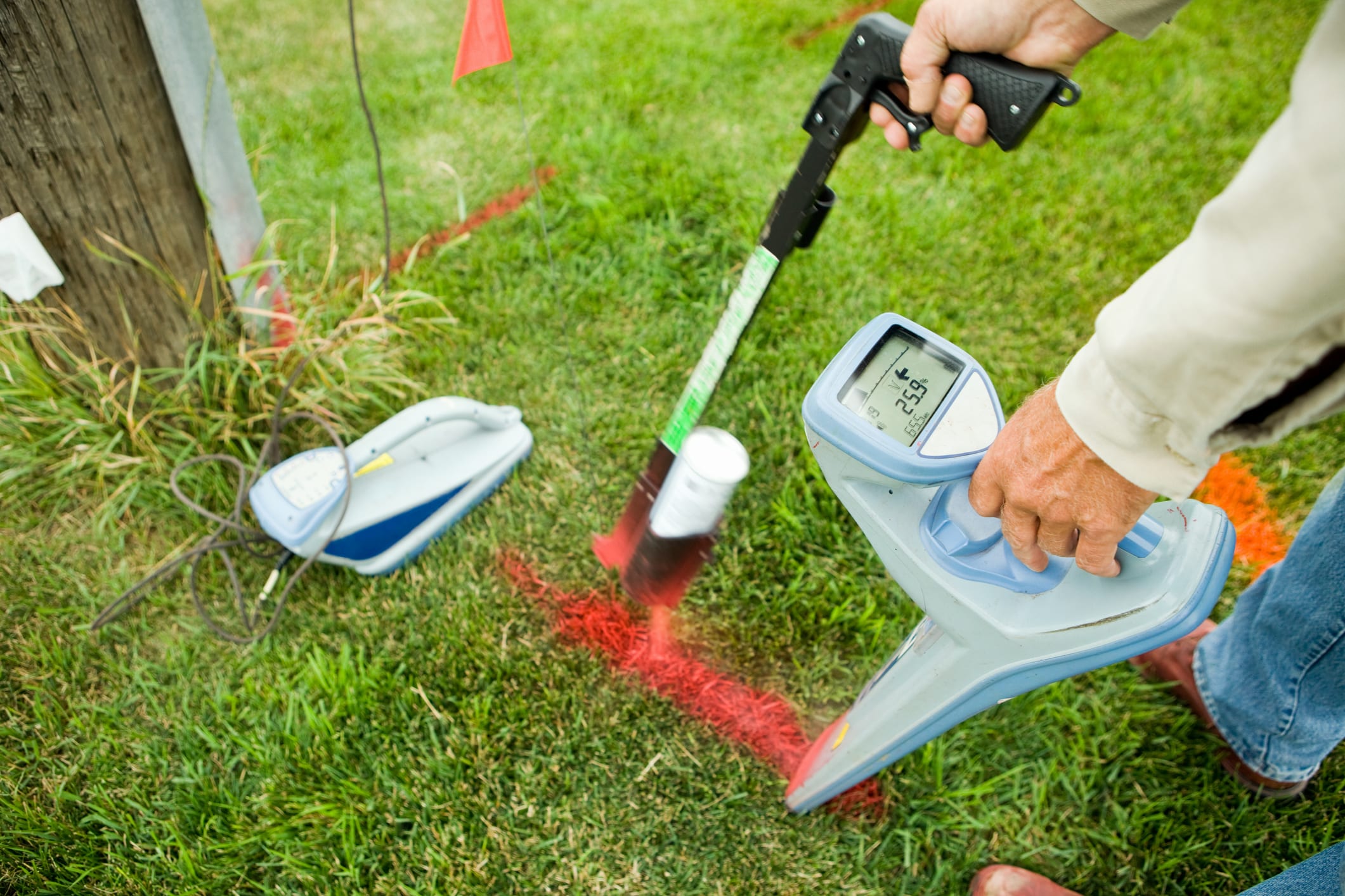 An electric utility worker is using a radio frequency detector to determine a buried power line location and mark it with spray paint and a red flag. The transmitter is to the left and is connected to the ground line from a utility pole. The can painter has some motion blur. This image represents all of the components as a result of,