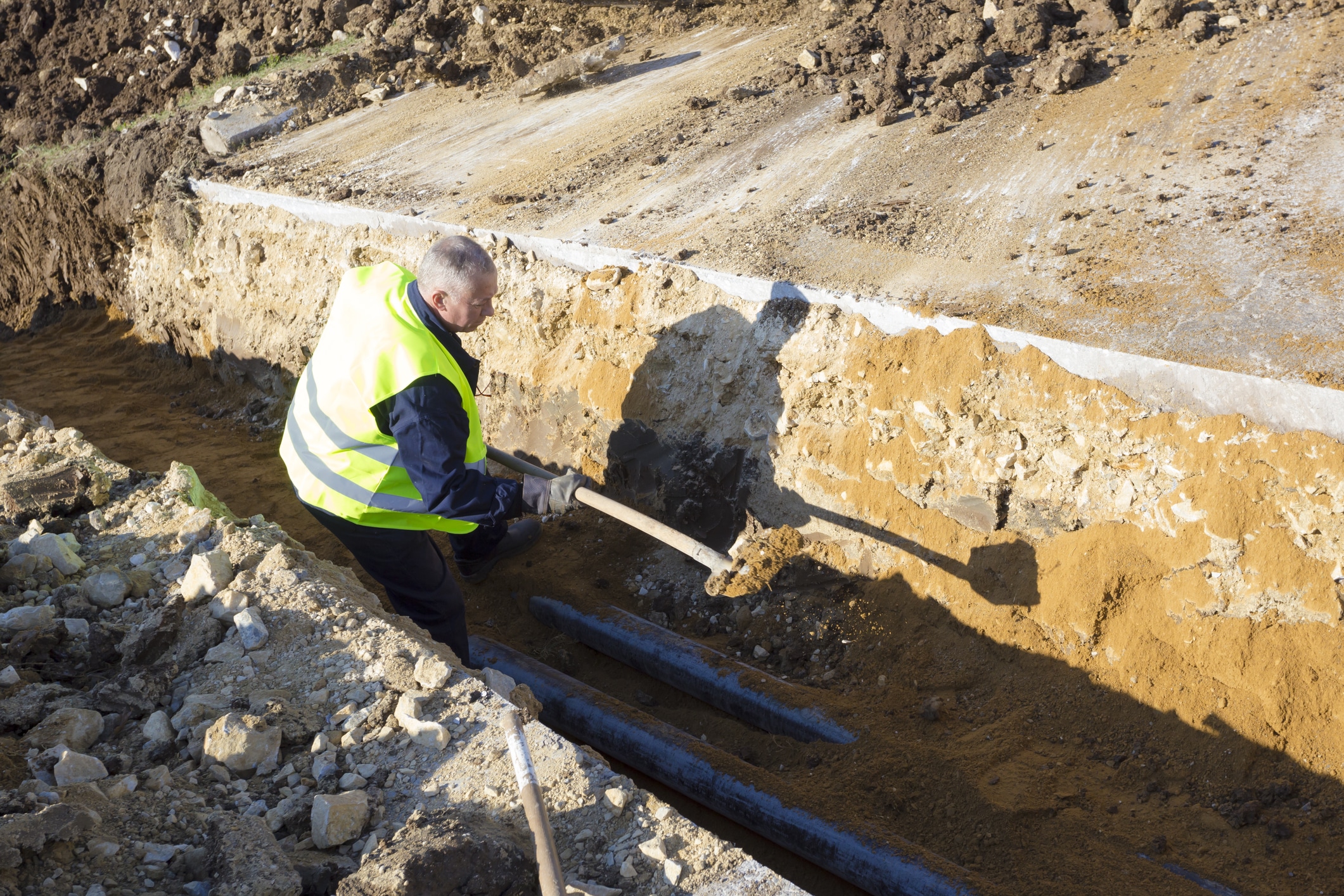 Worker works with shovel in a trench on pipeline construction site