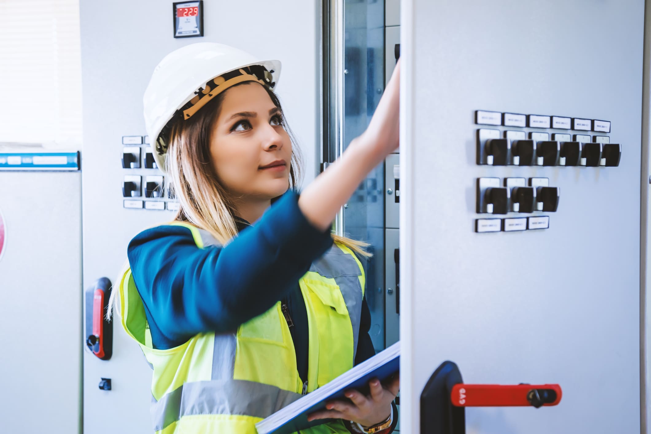 Young woman industrial service engineer wearing white helmet standing, working, checking conducts front of a control panel read and writing notes with digital tablet in energy control room of modern power plant electric energy station. XXXL size taken with Canon 5D MIV